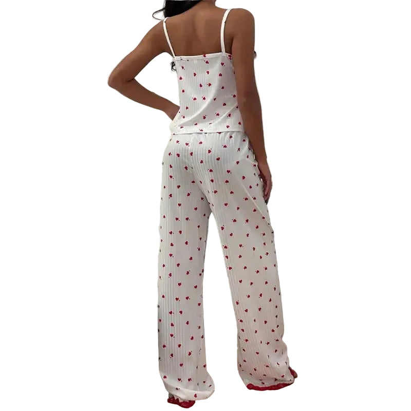 A woman wearing a white ribbed two-piece pajama set with a red heart pattern, photographed in a bedroom setting.