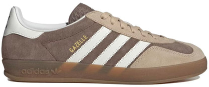 A side profile view of an Adidas Gazelle sneaker in brown suede and beige canvas, featuring white three-stripes, gold 'GAZELLE' text, and a translucent brown gum sole.
