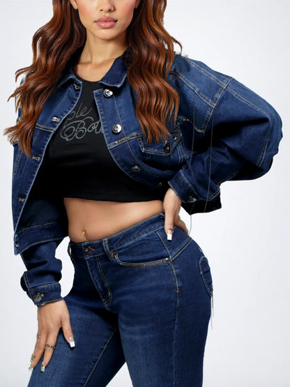 A woman wearing a cropped dark blue denim jacket over a black crop top and dark blue jeans, photographed against a light gray studio background.