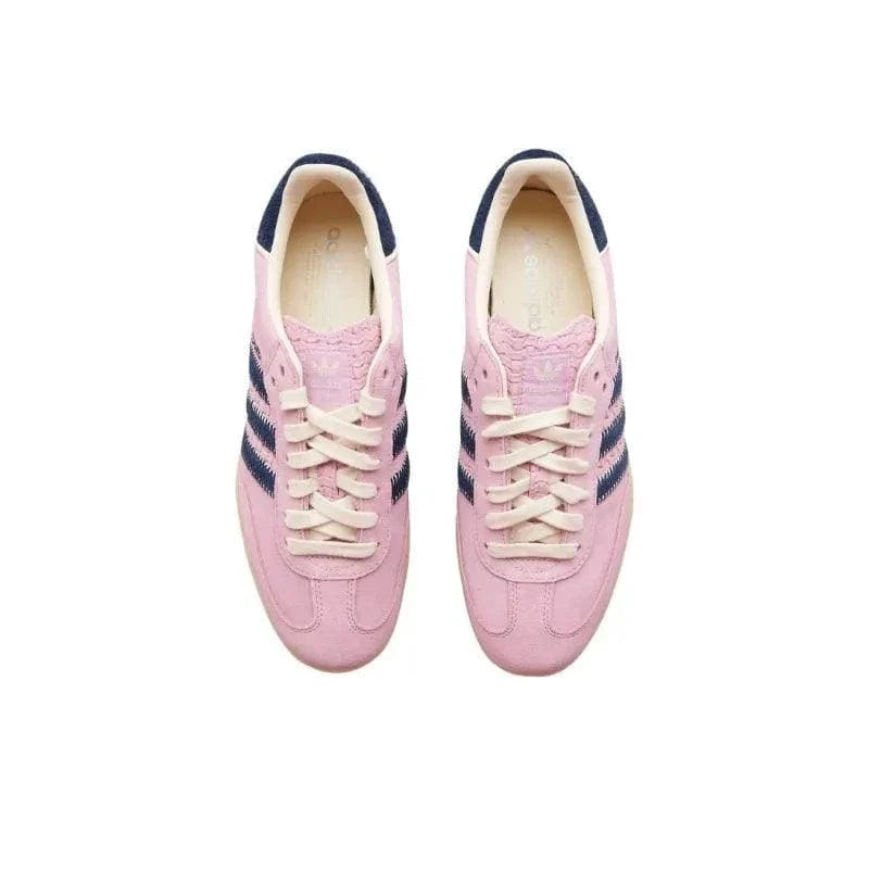 A pair of pink suede sneakers with navy blue stripes and cream laces, shown from a top-down view on a white background.