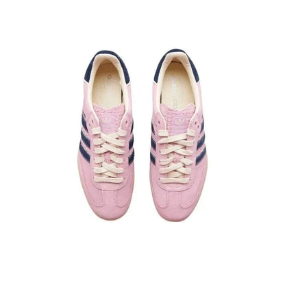 A pair of pink suede sneakers with navy blue stripes and cream laces, shown from a top-down view on a white background.