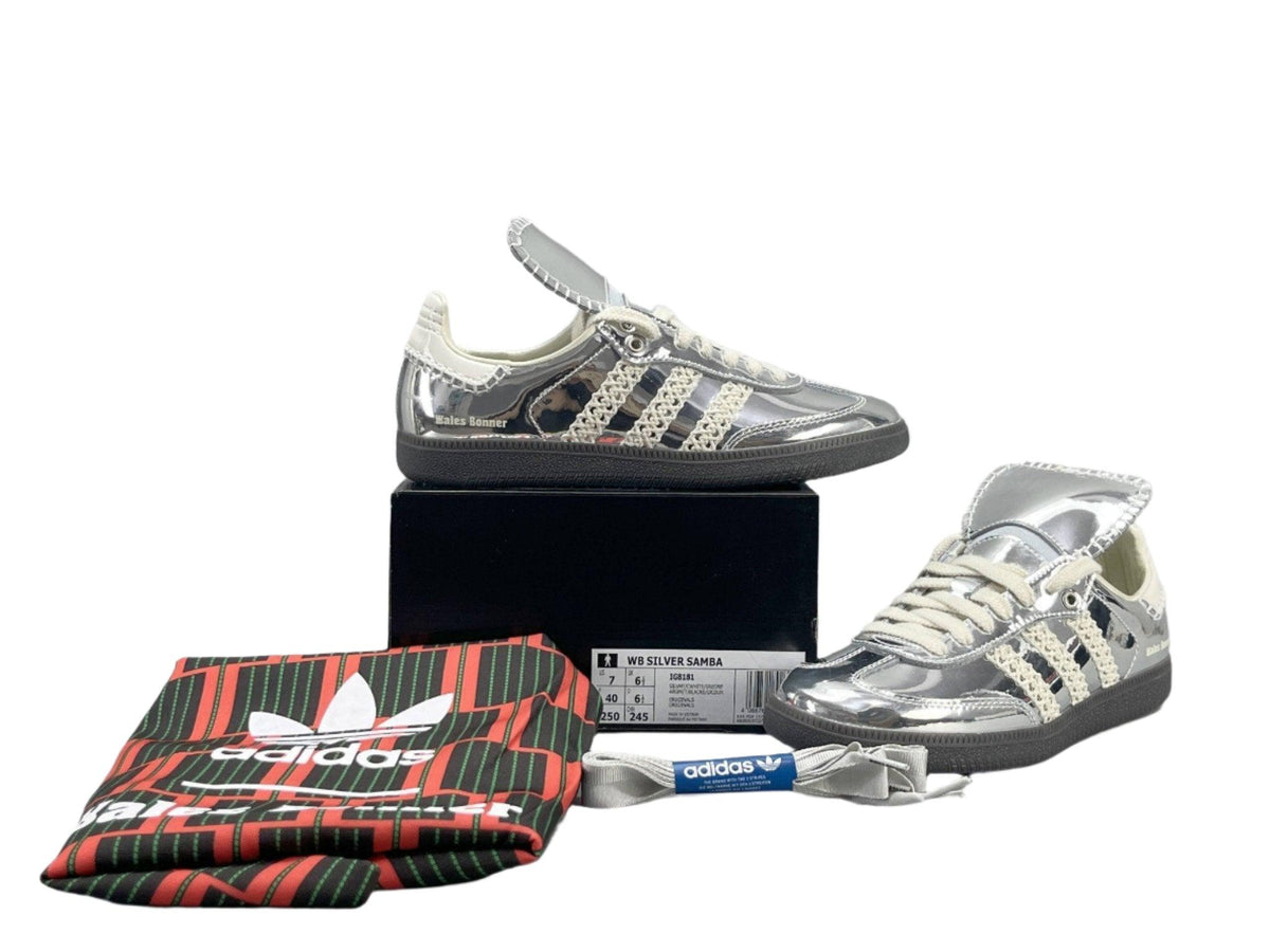 Silver Adidas sneakers with a black box and red and black Adidas wallet on a white background