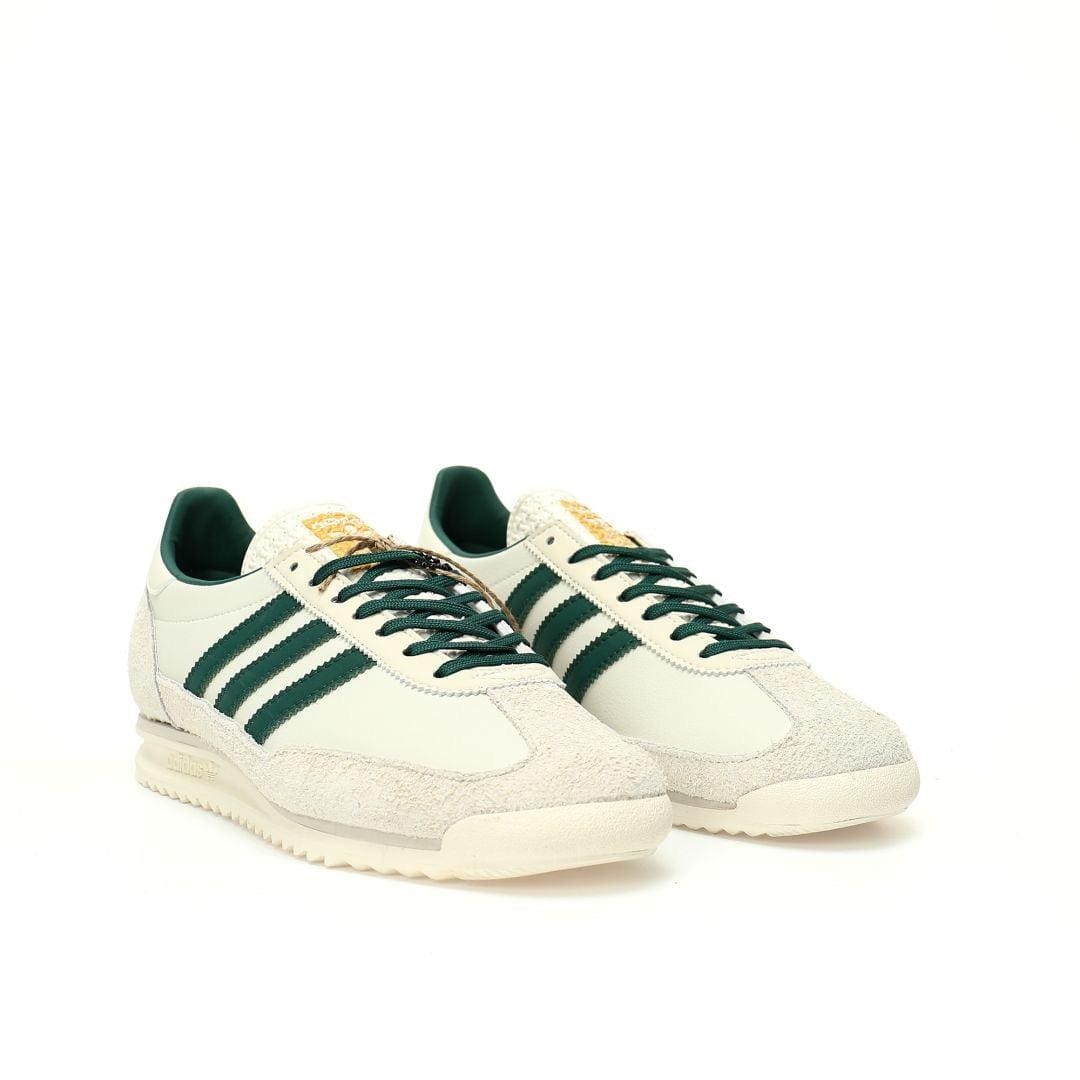 Pair of white sneakers with green stripes on a white background