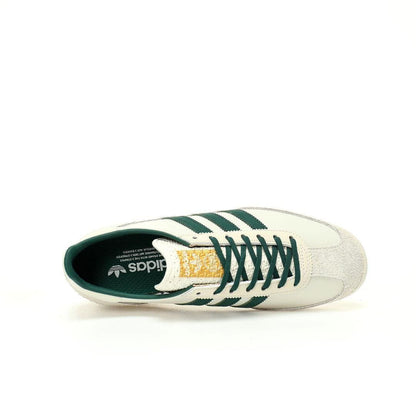 A single Adidas low-top sneaker shown from a side profile view against a solid white background. The shoe features an off-white leather upper with dark green stripes, a green tongue and collar, and a textured gold heel tab.