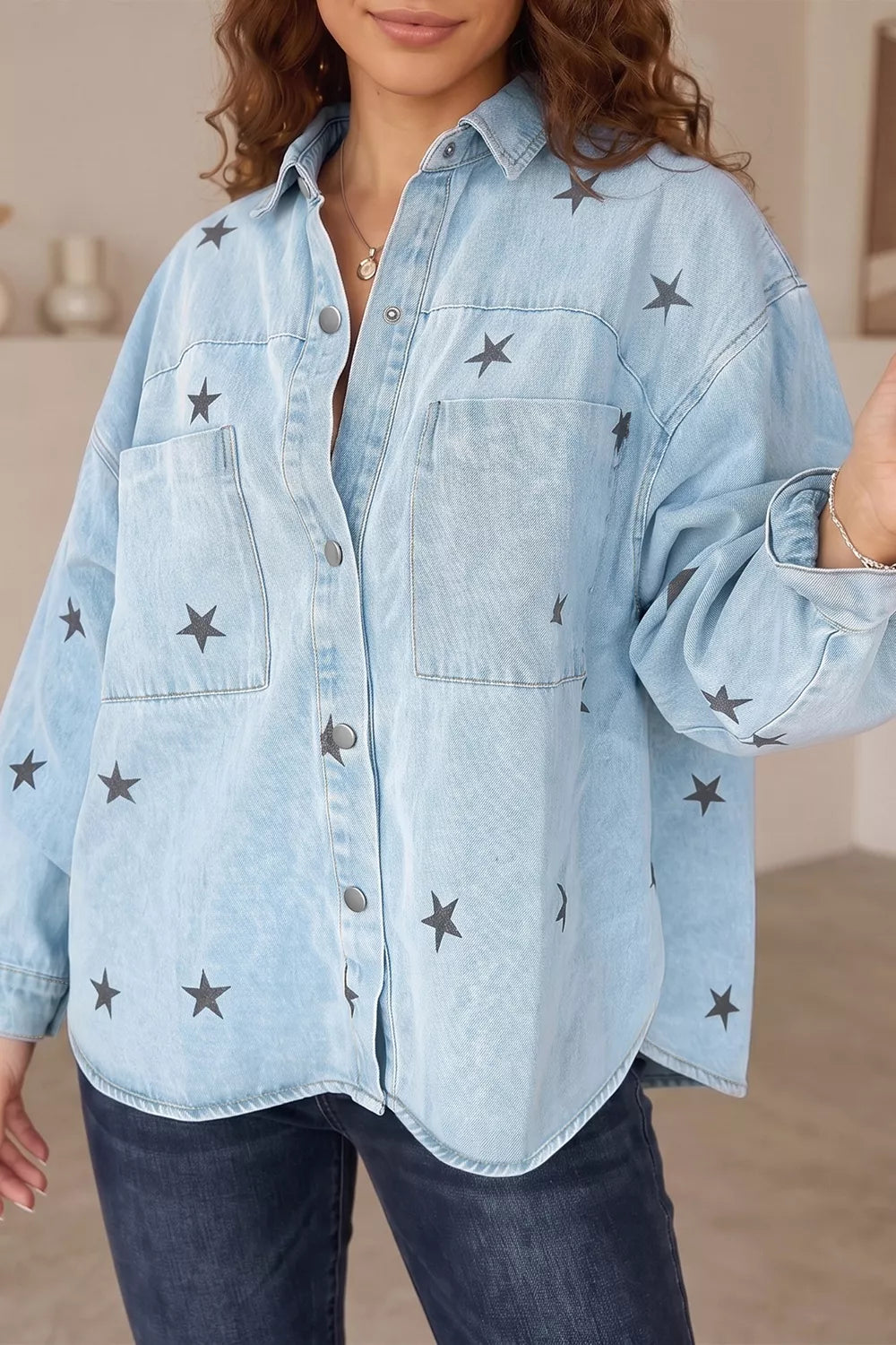 A woman wearing an oversized light blue denim button-up shirt with dark gray embroidered star patterns, paired with dark blue jeans.