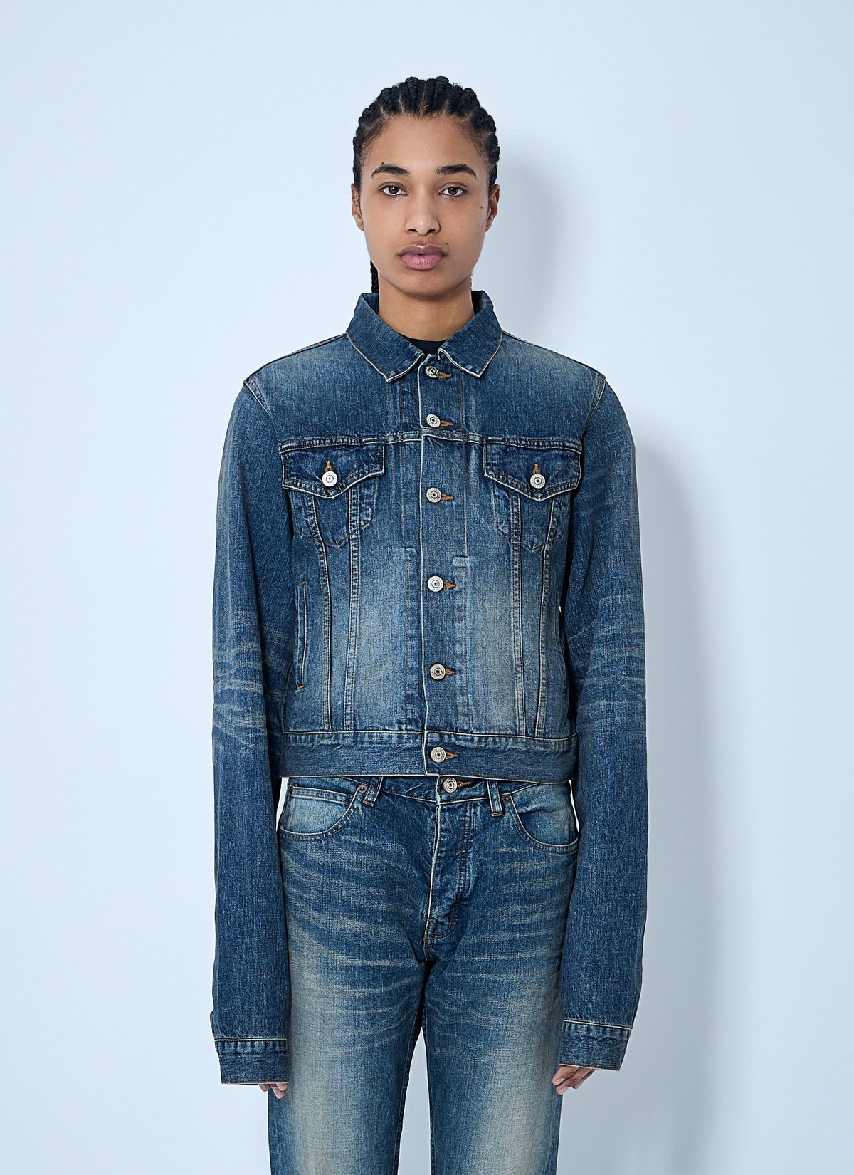 Person wearing a blue denim jacket and jeans against a light blue background