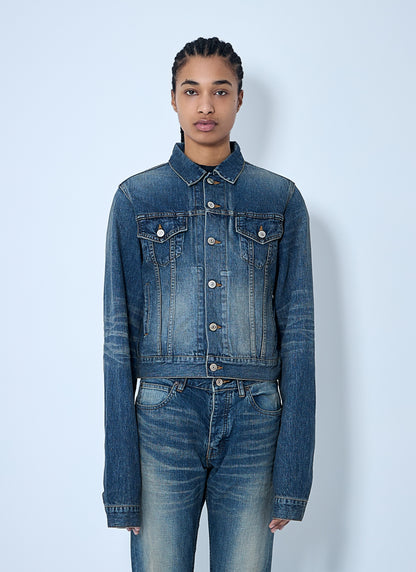 Person wearing a blue denim jacket and jeans against a light blue background