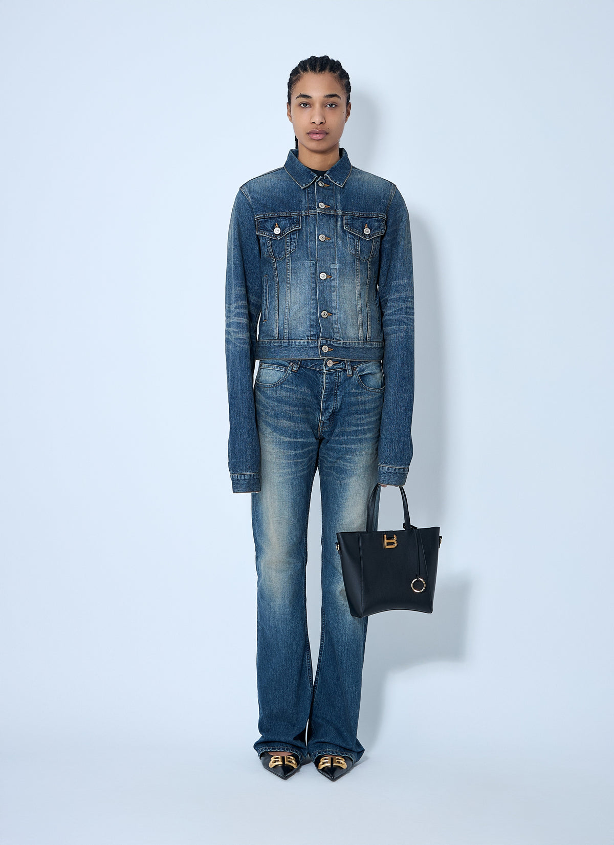 Person wearing a denim outfit with a black handbag on a light blue background