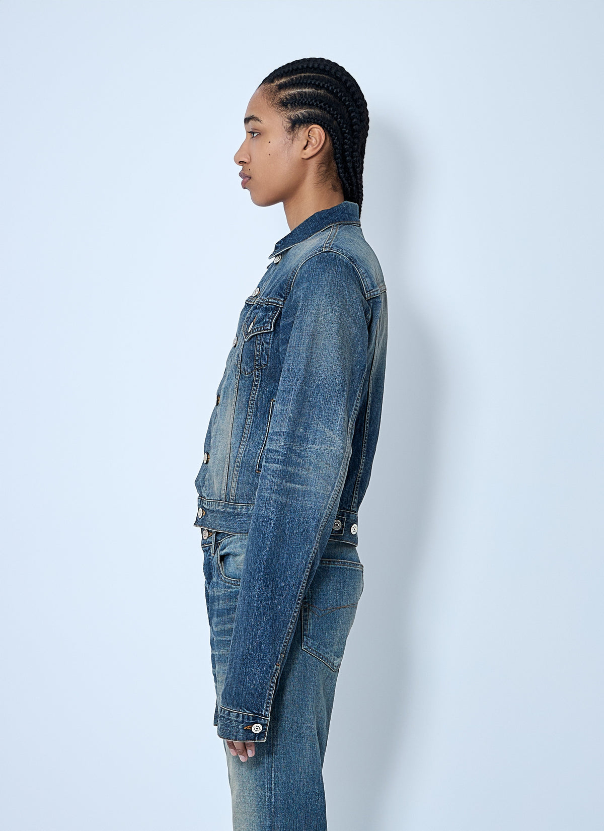 Person wearing a blue denim jacket and jeans against a white background
