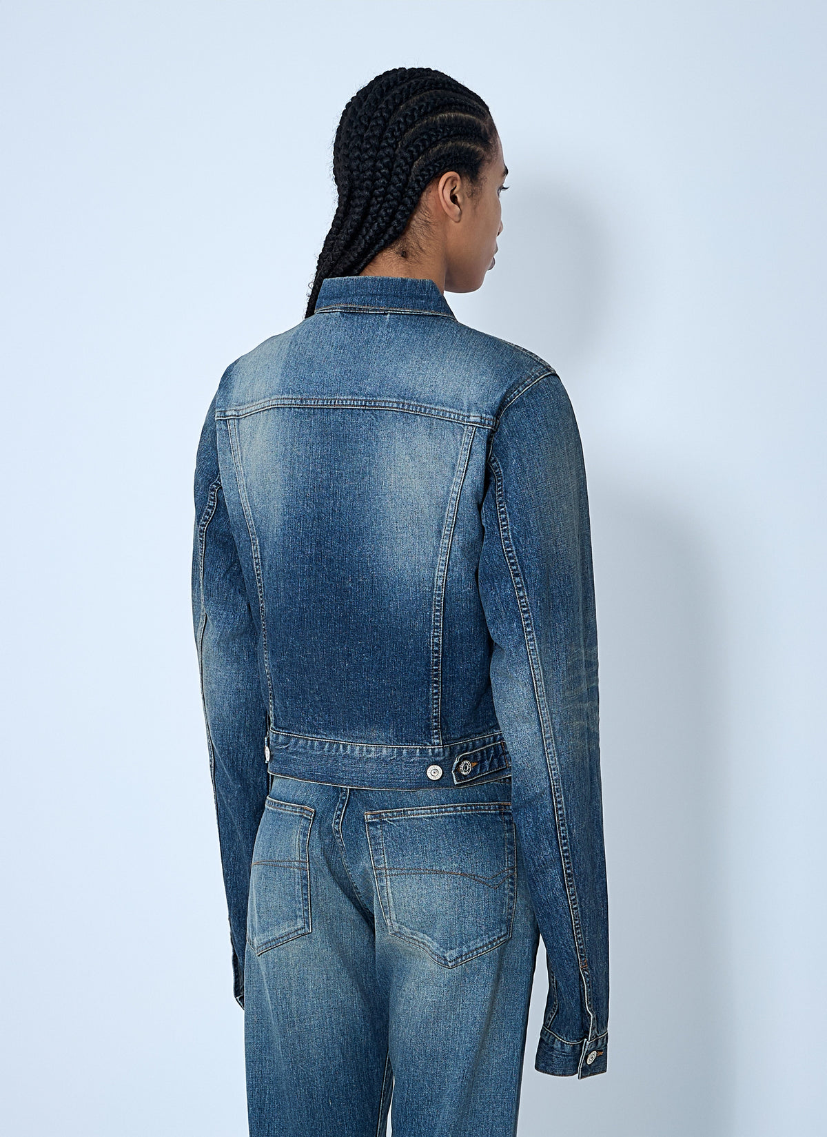 Person wearing a blue denim jacket and pants on a light gray background