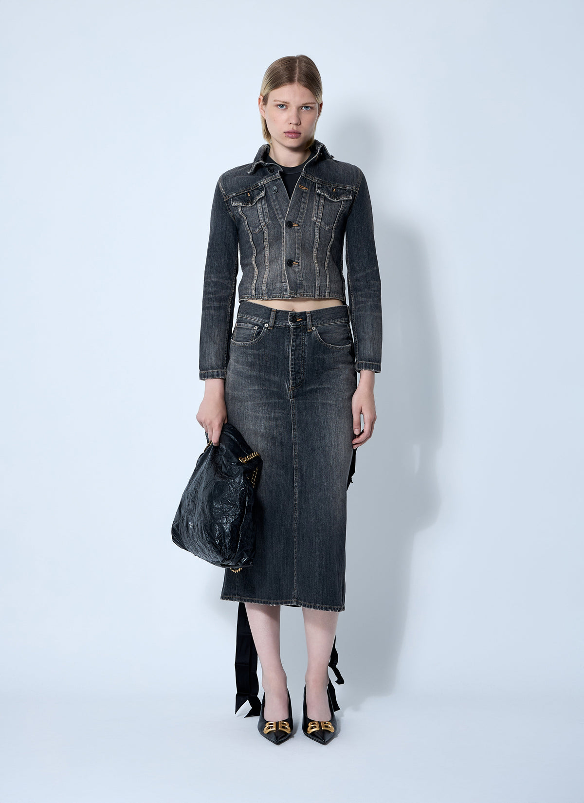 Woman wearing a denim outfit with jacket, skirt, and shoes against a white background