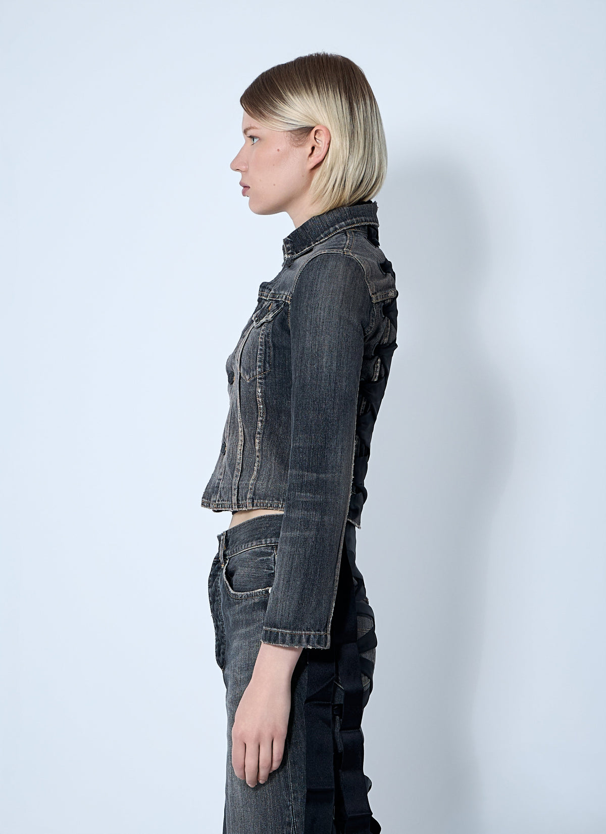 Person wearing a dark denim jacket and pants on a white background