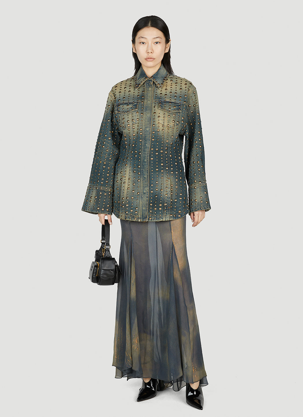 Woman wearing a patterned green shirt and skirt with a black handbag on a white background