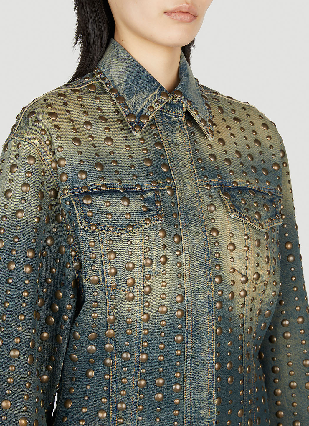 Denim jacket with gold studs worn by a person on a light gray background