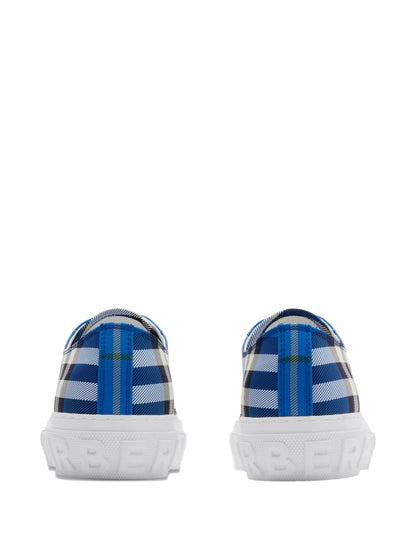 A pair of Burberry low-top sneakers shown from the back, featuring a blue, white, and gray tartan plaid pattern on the uppers and chunky white rubber soles with embossed branding.