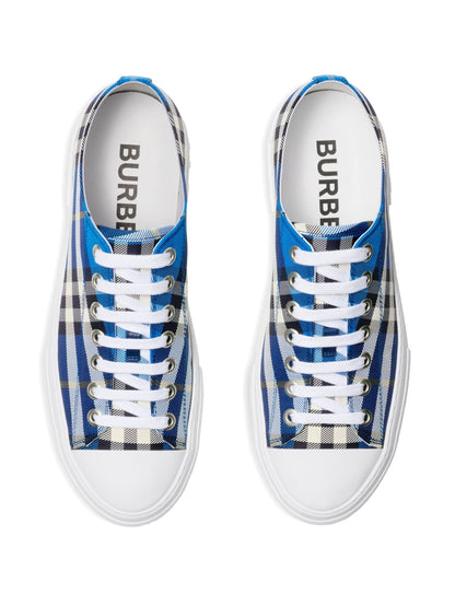 A pair of Burberry low-top sneakers shown from a top-down view. The shoes feature a blue, white, and black plaid pattern on the canvas uppers, white laces, and white rubber soles.