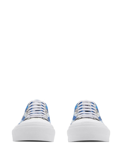A pair of low-top canvas sneakers shown from the front, featuring a white rubber sole and a blue, white, and gray patterned canvas upper with white laces, set against a plain white background.