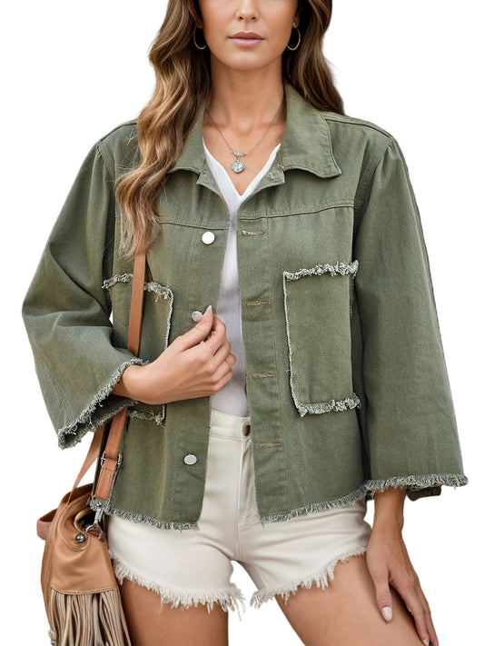 A woman wearing an olive green frayed-edge denim jacket over a white top and white frayed shorts, with a tan shoulder bag, standing in front of a dark wooden door.