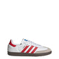 A white Adidas Samba sneaker with red three-stripes, a red heel tab, a beige suede toe cap, and a dark brown gum sole, shown from the side on a white background.