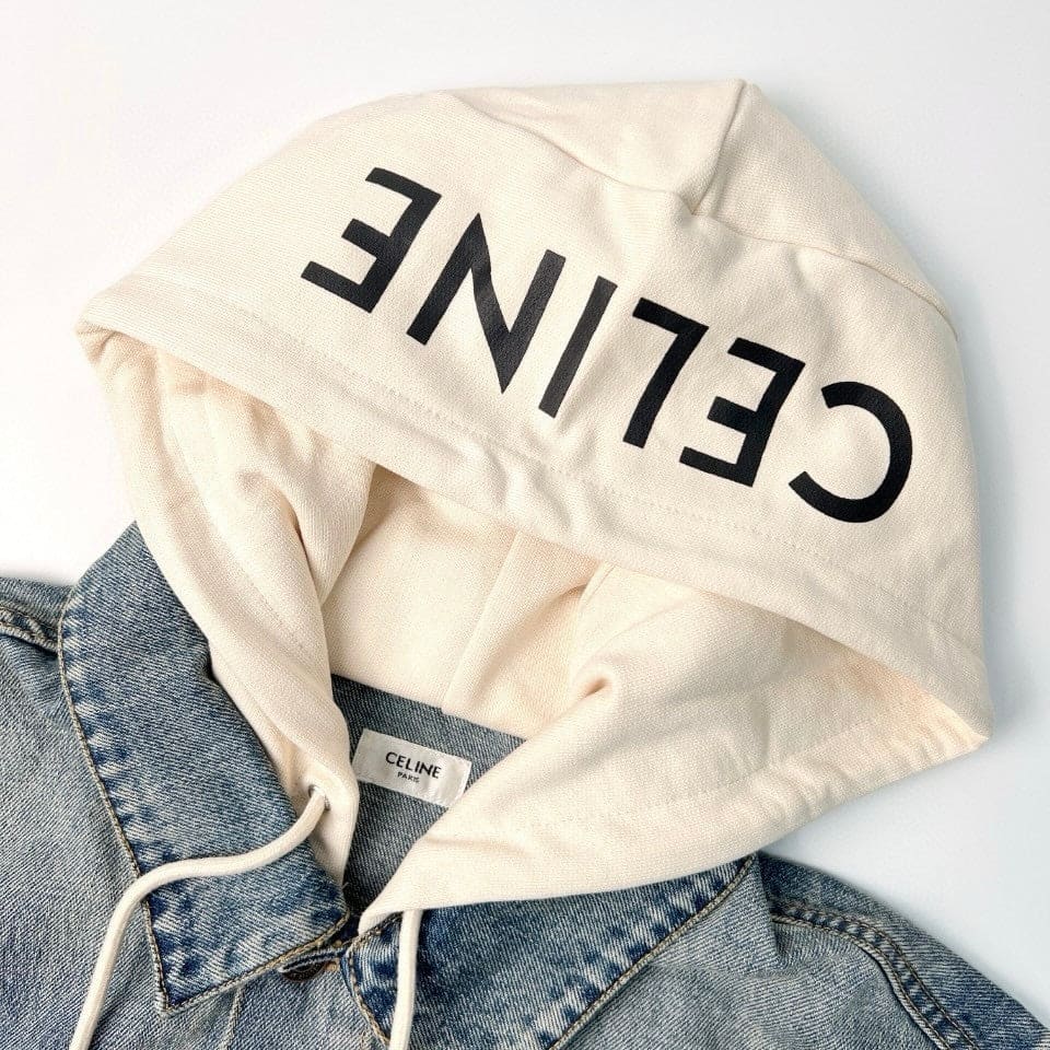 An off-white Celine hoodie with large black text on the hood, styled over a blue denim jacket against a white background.