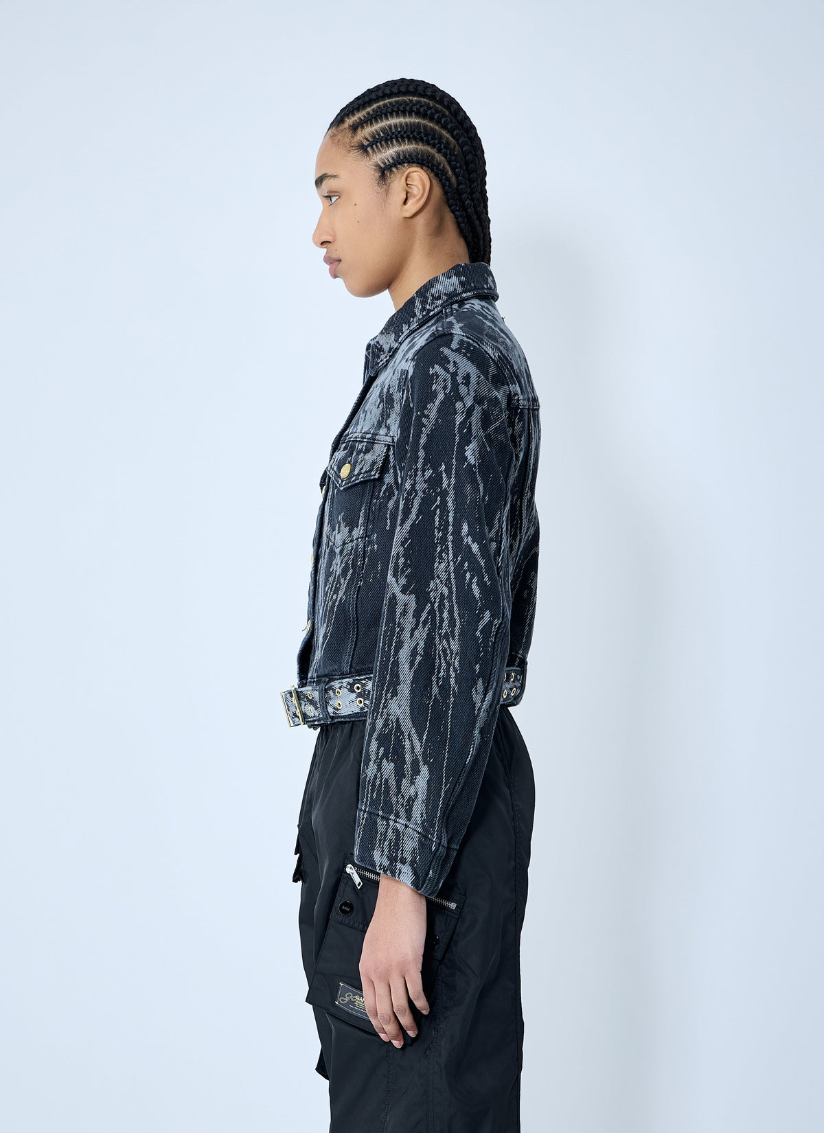 Person wearing a dark, patterned jacket and black pants on a white background