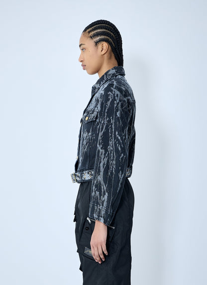 Person wearing a dark, patterned jacket and black pants on a white background
