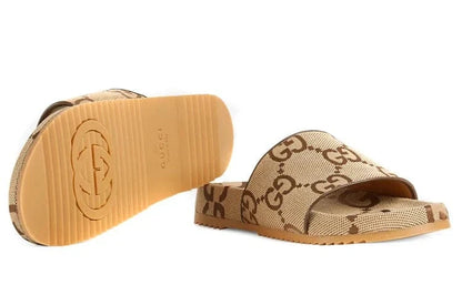 Gucci slide sandals in beige GG monogram canvas with a tan rubber sole, shown on a white background with one sandal displaying the sole.