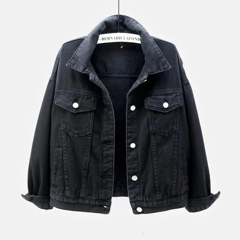 A black washed denim jacket hanging on a hanger against a light gray background. The jacket features a classic collar, a button-up front, and two buttoned chest pockets.
