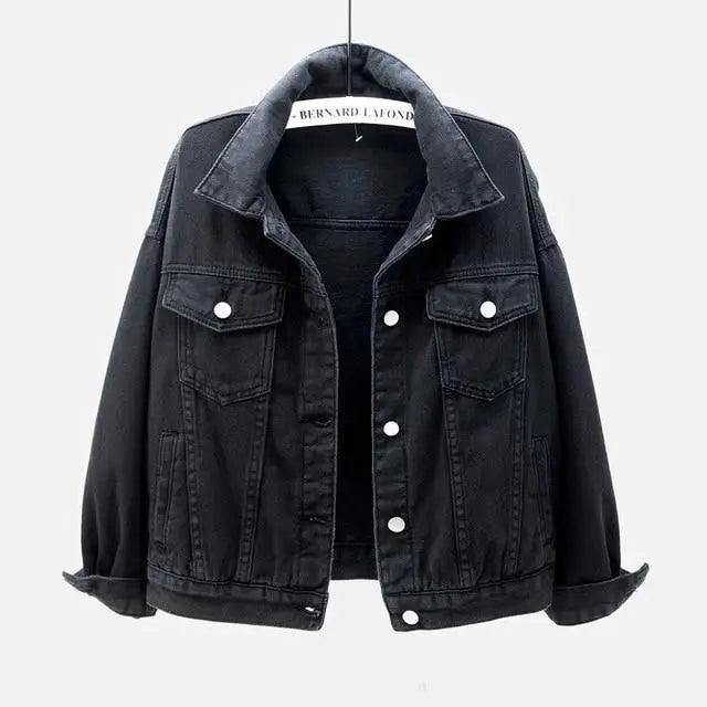 A black washed denim jacket hanging on a hanger against a light gray background. The jacket features a classic collar, a button-up front, and two buttoned chest pockets.