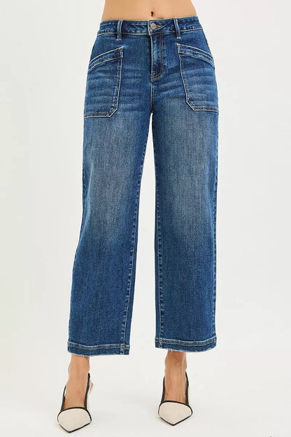 A model is wearing a pair of high-waisted, wide-leg cropped blue denim jeans with a faded wash, paired with black and white pointed-toe heels, against a plain white studio background.