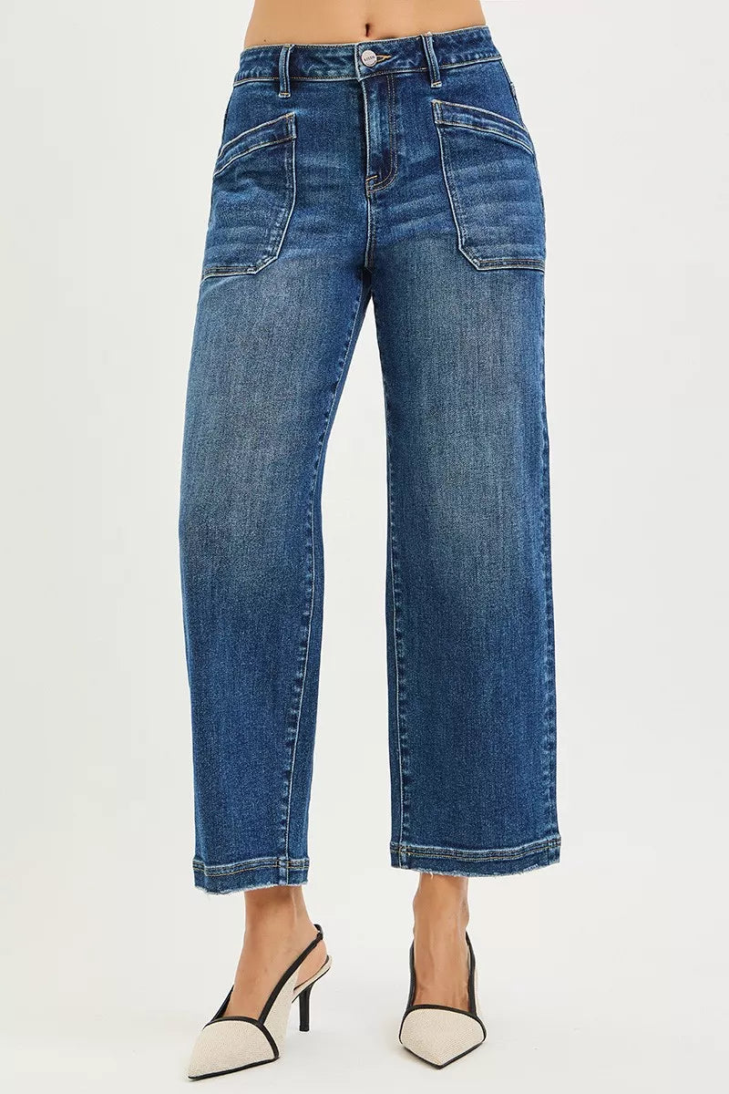 A model is wearing a pair of high-waisted, wide-leg cropped blue denim jeans with a faded wash, paired with beige and black pointed-toe heels, shot against a plain white studio background.