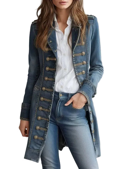 A woman wearing a long blue denim military-style coat with large gold-tone buttons over a white button-up shirt and blue jeans, photographed against a light gray studio background.