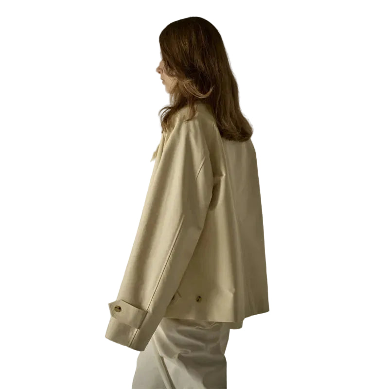 A woman shown from the back wearing an oversized cream-colored blazer and matching cream trousers, standing against a plain light gray studio background.